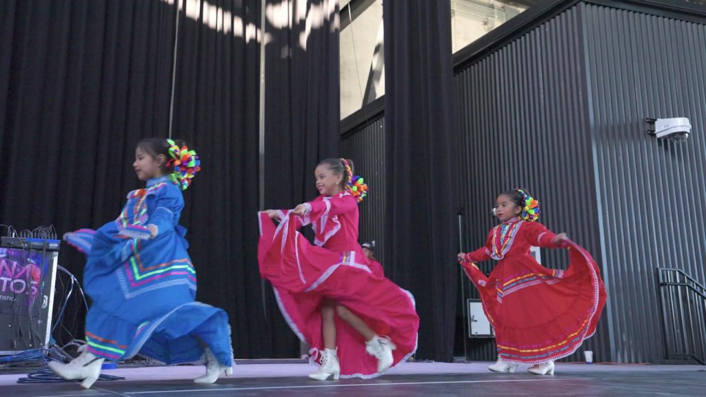 Young folklórico dancers in blue, pink and red skirts performing on stage at La Fiesta Hispana at VyStar Pavilion in Port Wentworth, GA