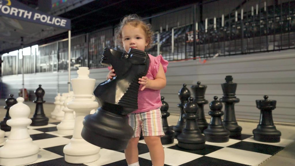 Toddler holding a giant black chess knight on the oversized chess board at VyStar Pavilion