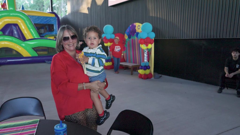Grandmother holding a smiling toddler in the kids' zone at La Fiesta Hispana in Port Wentworth