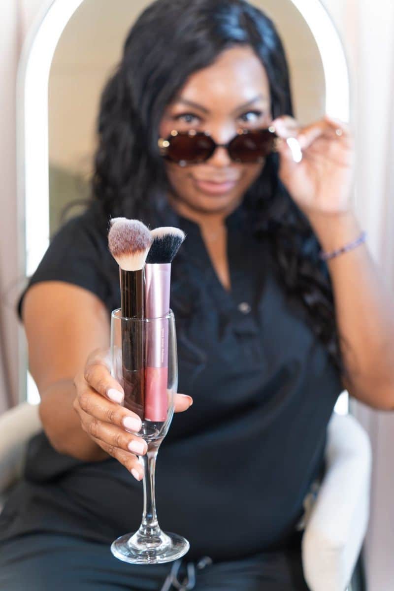Brand portrait by Coastal Moss Creative of a makeup artist holding makeup brushes in a champagne flute